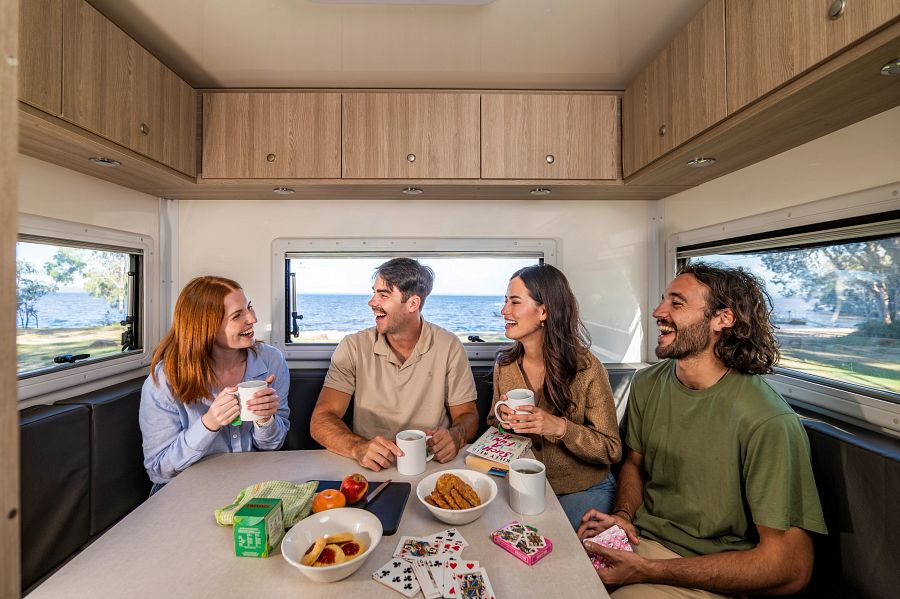Twee stellen zitten in de zithoek van een camper met koffie en thee in de hand en een kaartspel