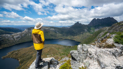 Man in gele regenjas kijkt uit over een meer in Cradle Mountain