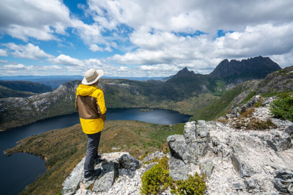 Man in gele regenjas kijkt uit over een meer in Cradle Mountain