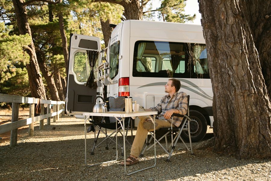 Man zit buiten aan de campingtafel bij een Mighty camper op een camping in Picton