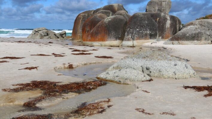 Zicht op grote rode rotsblokken en de zee op Sqeaky Beach in Wilsons promontory