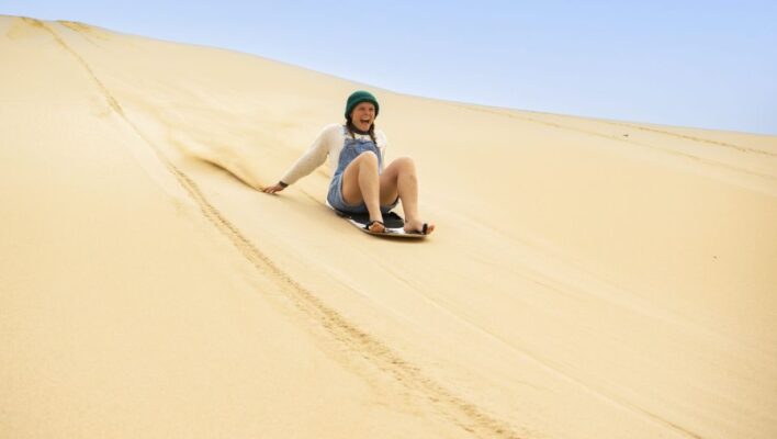 Gillende vrouw surft op sandboard naar beneden op zandheuvel in Port Lincoln