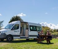 Vader, moeder en kind zitten aan picknicktafel voor de Maui Ultima Plus camper bij Lake Taupo in Nieuw-Zeeland