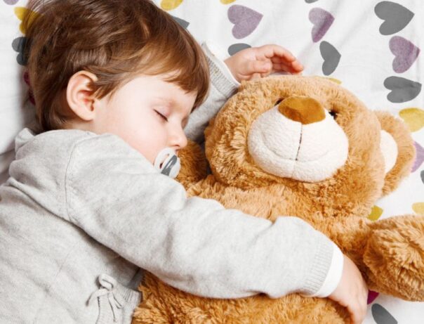 Kind slaapt met teddybeer en speen in de mond