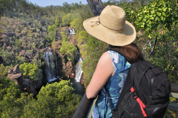 Vrouw met hoed op en rugzak op rug kijkt naar Florence Falls in Litchfield National Park