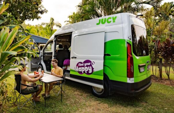 Jucy Coaster staat op een campingplaats met de voor, - en zijdeur open, twee mannen zitten buiten aan tafel