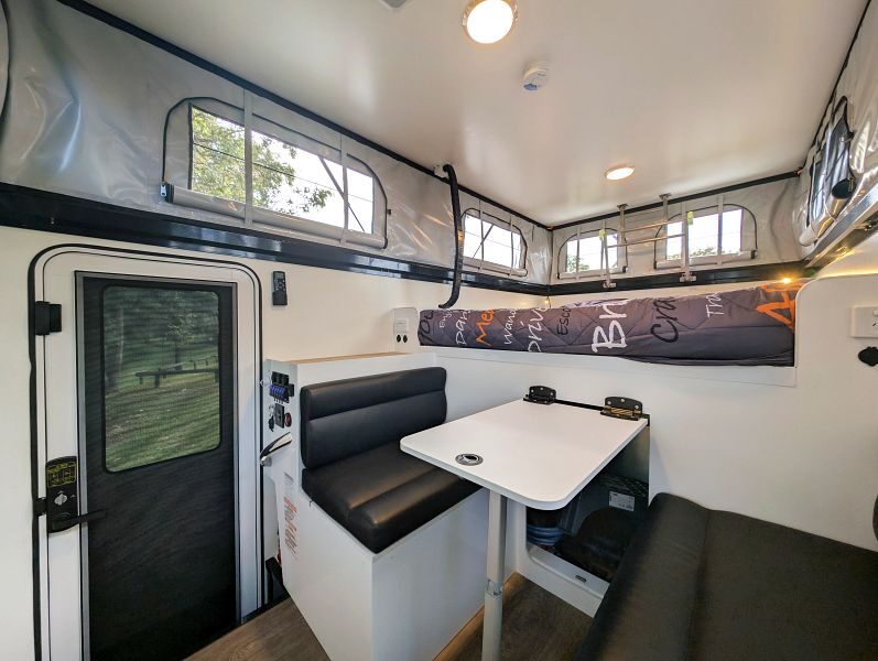 Zicht op het interieur van de Britz Maverick 4WD met deur, tafel bankje en tweepersoons bed