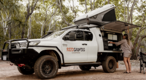 De vrouwelijke camperreiziger is bezig een maaltijd te bereiden in het keukengedeelte aan de zijkant van de RedSands 4WD camper