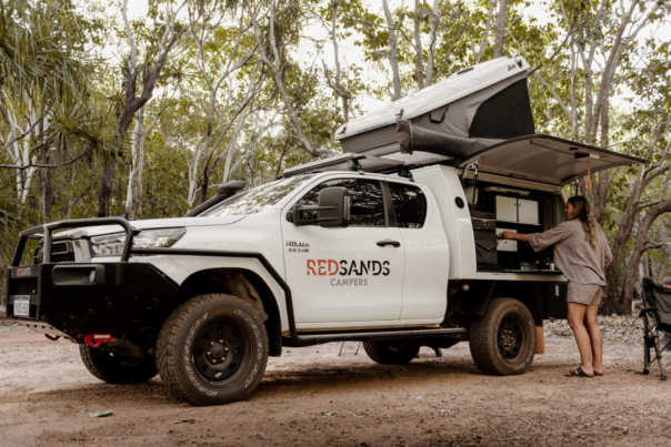 De vrouwelijke camperreiziger is bezig een maaltijd te bereiden in het keukengedeelte aan de zijkant van de RedSands 4WD camper