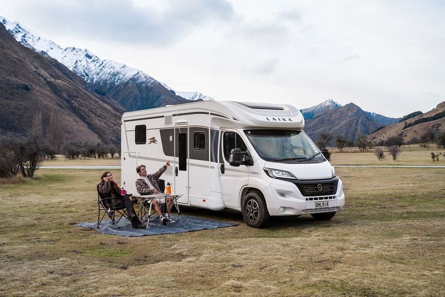 Koppel zit op de campingstoelen aan tafel buiten de Britz Odyssey camper in de bergen van Nieuw-Zeeland