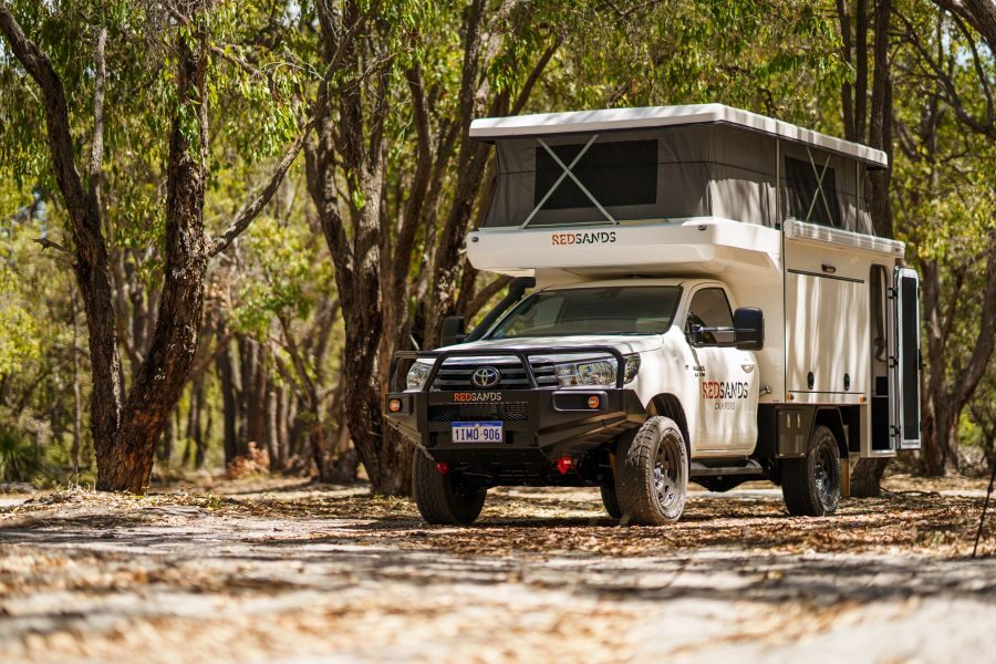 De RedSands camper met uitgeklapt dak staat in een schaduwrijke plek tussen de bomen