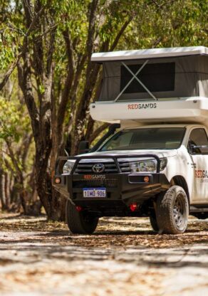 De RedSands camper met uitgeklapt dak staat in een schaduwrijke plek tussen de bomen