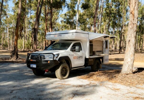 De camper is geparkeerd op een plek tussen de bomen - de klep aan de zijkant is geopend met een uitschuifbaar keukenwerkblad