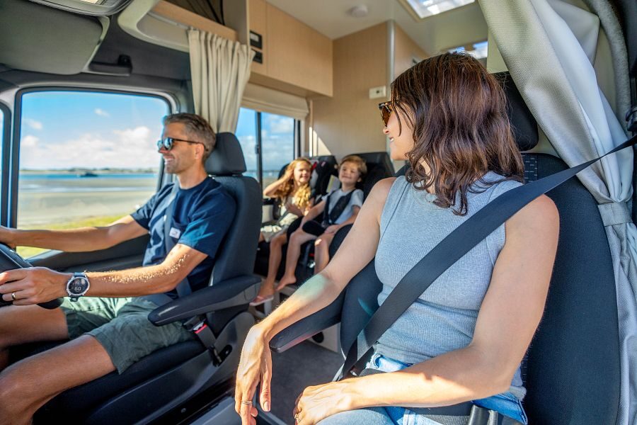 Een gezin is aan het rijden in de Maui Cascade camper waarbij je de twee kinderen achterin ziet zitten in de kinderstoelen