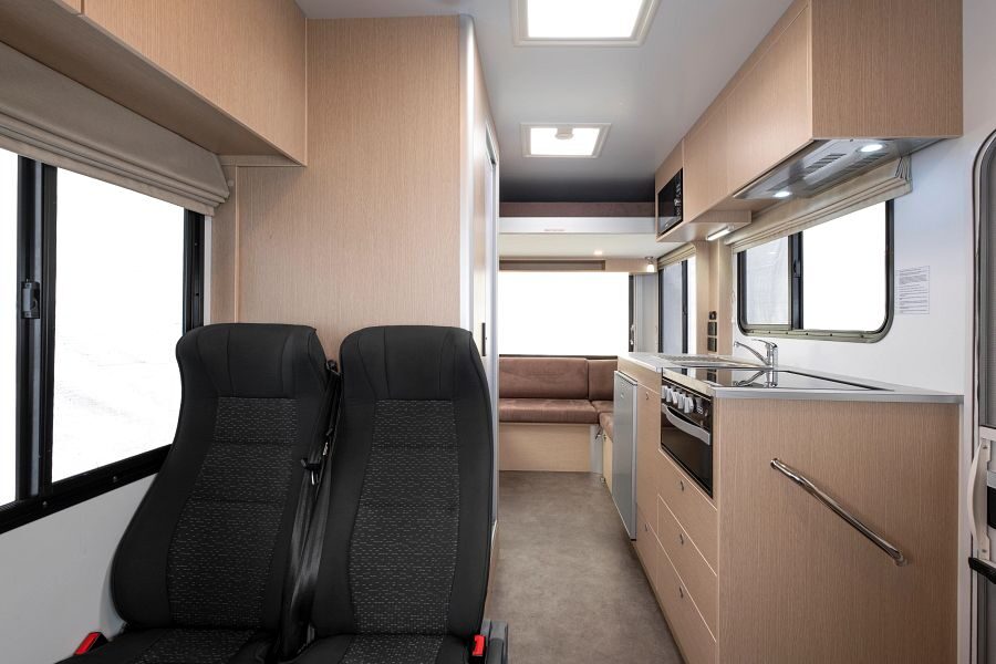 Twee zitplaatsen achter de bestuurdersruimte gezien vanuit de cabine met zicht op de keuken en de zithoek achterin de camper