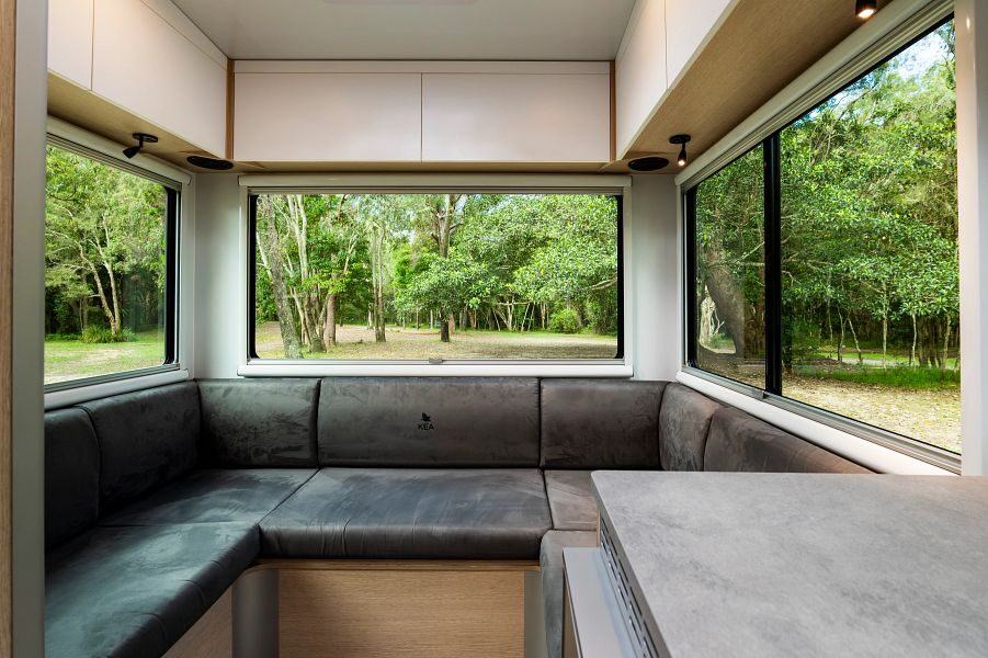 De ruime zithoek achterin de Maui Beach camper met grote ramen met uitzicht op de groene natuur