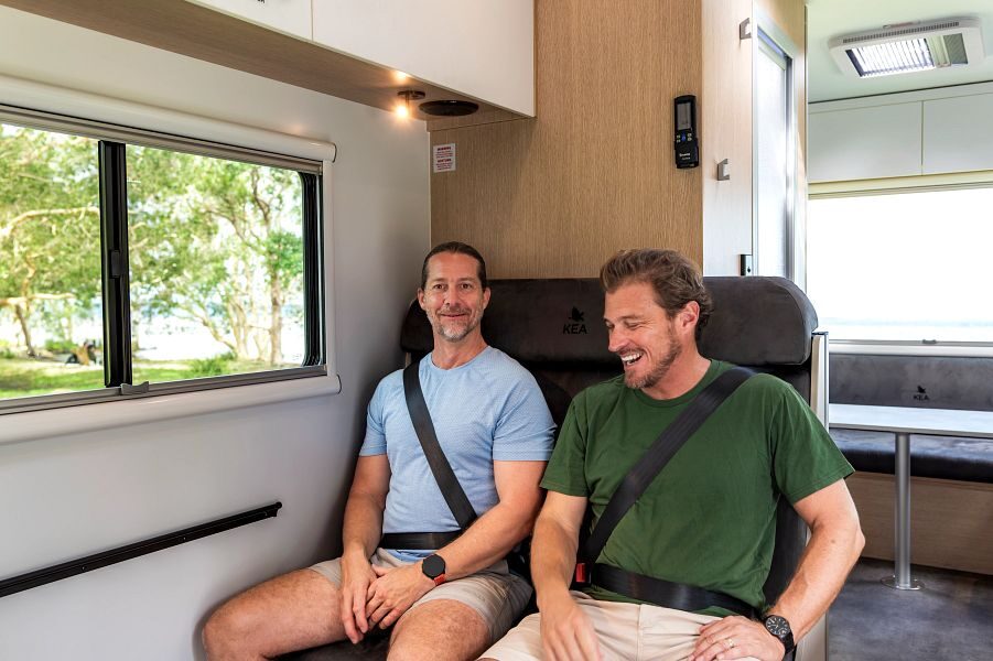 Twee mannen zitten op de zitplaatsen achter de bestuurdersruimte met de gordels vast in de Maui Beach camper