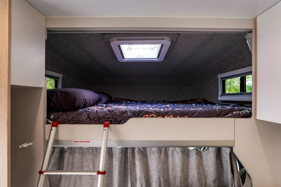 Het tweepersoonsbed in de alkoof met ramen en een ladder in de Maui River camper