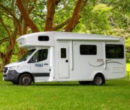 De zijkant van de Maui River camper voor zowel Australië als Nieuw-Zeeland geparkeerd op een grasveld onder een boom