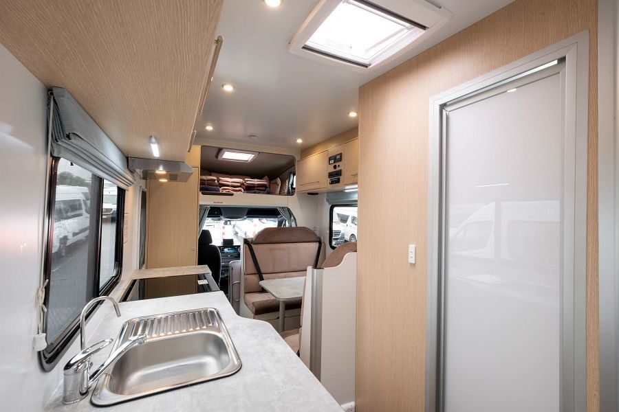 Het interieur van de Maui River camper vanuit de achterkant van de camper met zicht op de keuken, de zithoek in het midden van de camper en de deur van de badkamer