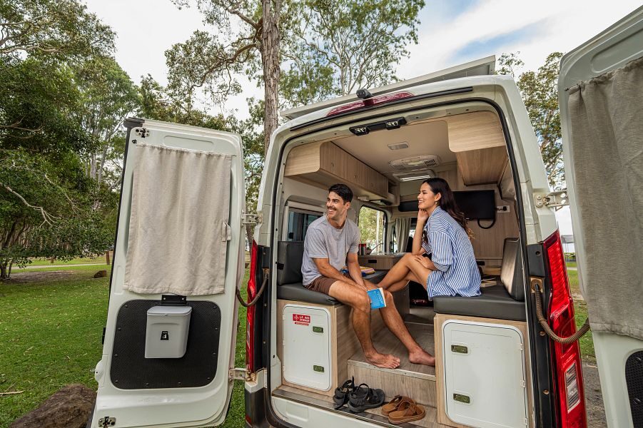 Een koppel zit in de achterkant van de Mighty Highball camper en kijken via de openstaande achterdeuren naar buiten