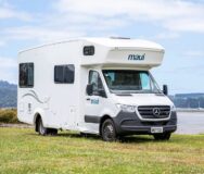De Maui Sunset camper vanaf de voor- en zijkant geparkeerd langs het water op het gras in Australië