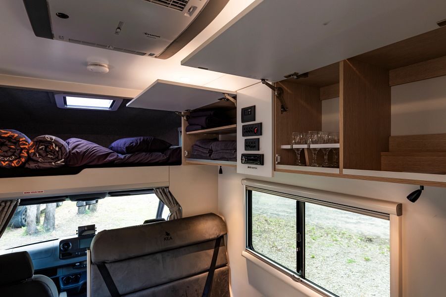 De kasten boven het zitgedeelte in de midden van de Maui Sunset camper staan open en daarachter is het tweepersoonsbed in de alkoof