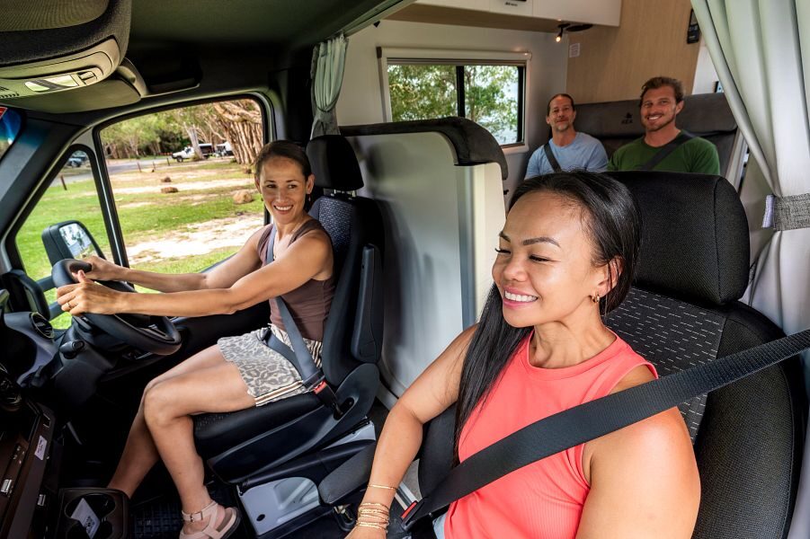 Een vriendengroep van 4 personen zijn aan het rijden in de Maui Sunset camper waarbij twee vrouwen en de bestuurdersruimte zitten en twee mannen op de zitplaatsen erachter