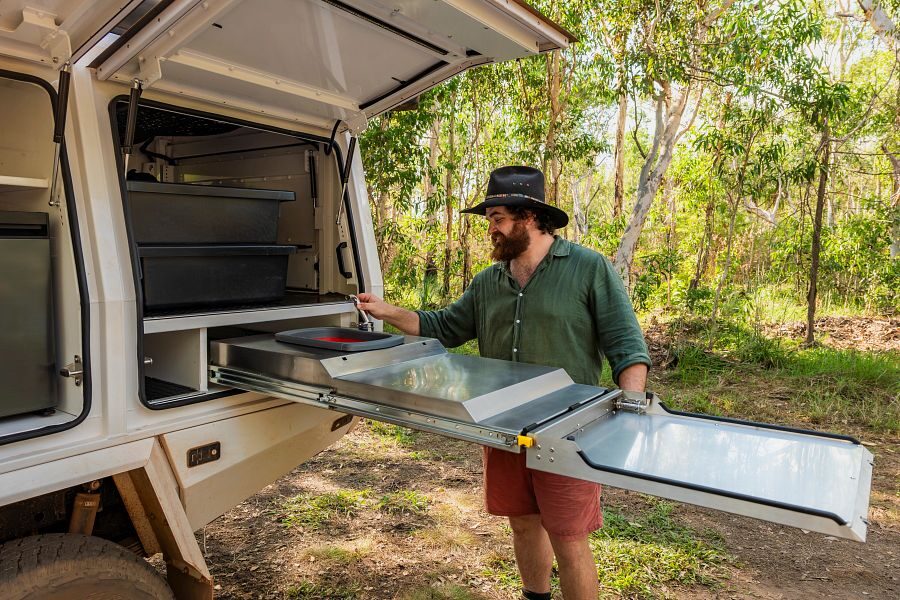 Een man schuift de buitenkeuken uit van de Apollo 4WD Overland Camper in Australië