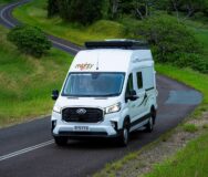 Een vrouw rijdt in de Mighty Double Down camper met daktent over een slingerende asfalt weg