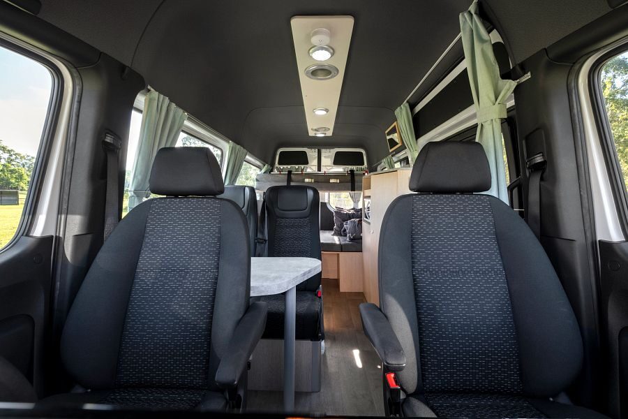 Het interieur met de zitplaatsen in en achter de cabine van de Mighty Double Down camper kijkend van voor naar de achterkant van de camper