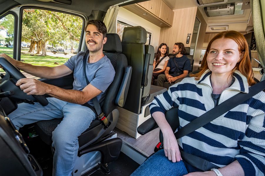Een man en vrouw zitten in de cabine en twee vrienden zitten erachter op de zitplaatsen van de Mighty Double Up camper terwijl ze rijden