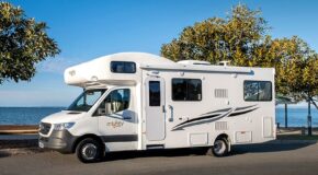 De zijkant van de Mighty Big Six camper die geparkeerd staat op een weg aan het water
