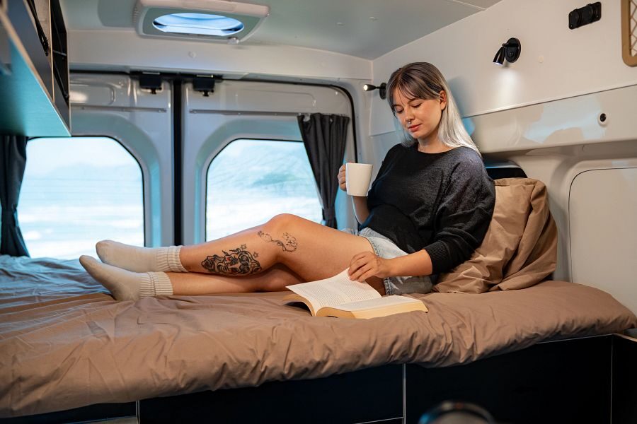 Een vrouw leest een boek op het tweepersoonsbed in de Mighty Lite HiLITE camper in Nieuw-Zeeland