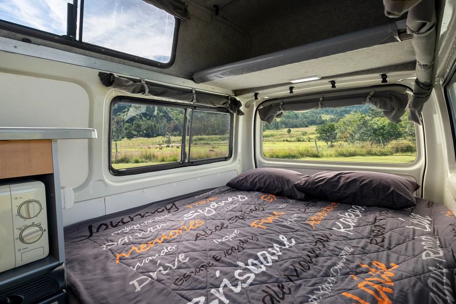 Het bed achterin de Mighty Lite HiLITE camper met uitzicht op de natuur van Australië