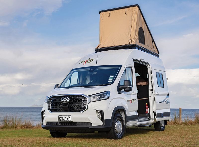 De Mighty Lite DeLITE camper staat geparkeerd op een grasveld met de daktent uitgeklapt en de zijdeur open in Nieuw-Zeeland