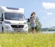 Een stel staat schuin voor de McRent Kiwi Compact camper te genieten van het uitzicht