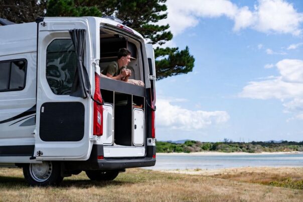 Man ligt op het bed van de Apollo Hitop camper met de achterdeur open en kijkt naar buiten