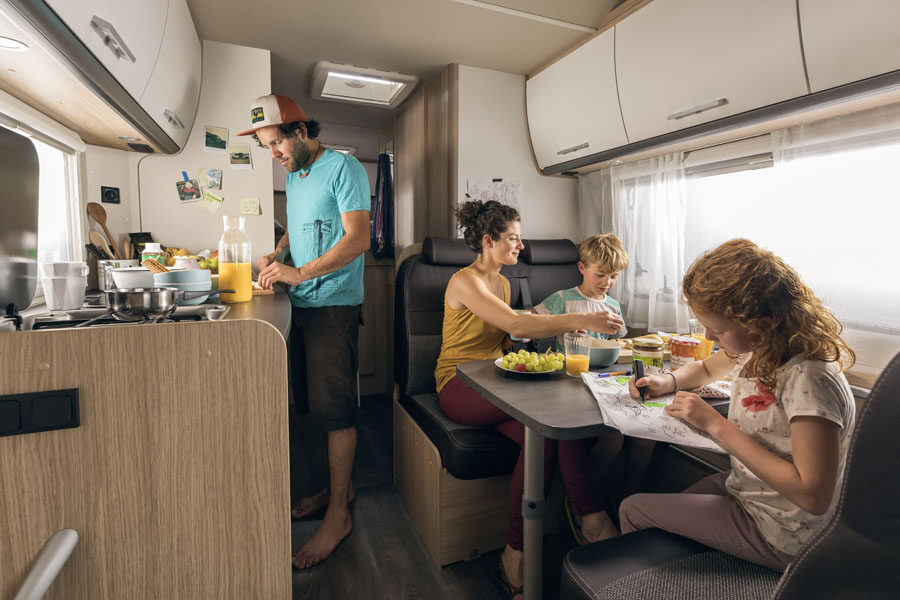 Een man is aan het koken in de keuken van de McRent Family Luxury camper terwijl zijn gezin aan tafel zit