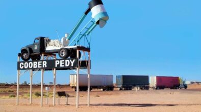 Plaatsnaambord van Coober Pedy met mijnbouw wagen erop en vrachtwagen op de achtergrond