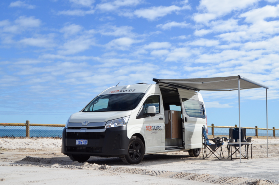 De RedSands camper op het strand met de zijdeur geopend en de campingtafel en stoelen onder de uitgeklapte luifel