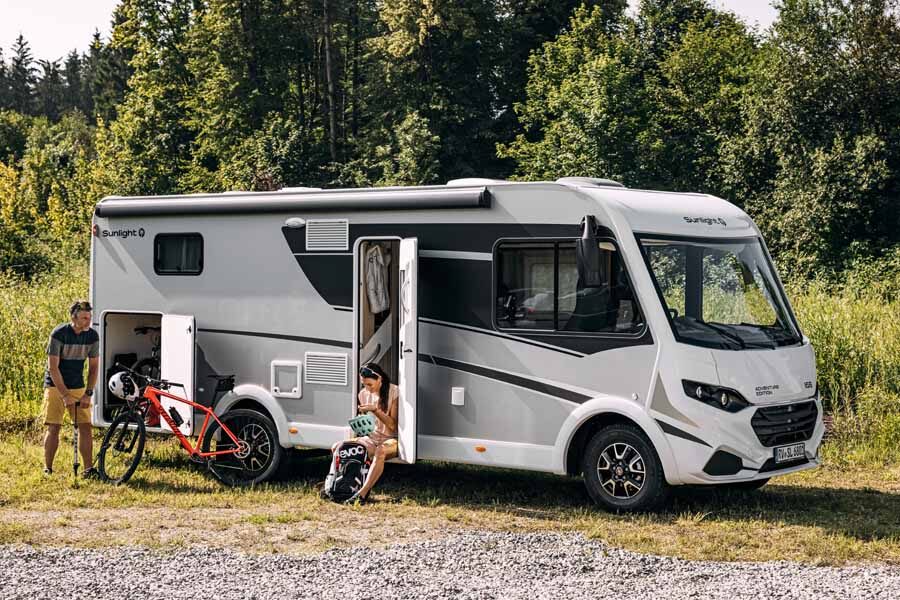 Een vrouw zit in de deuropening van de McRent Comfort Luxury terwijl haar man de band van zijn fiets oppompt