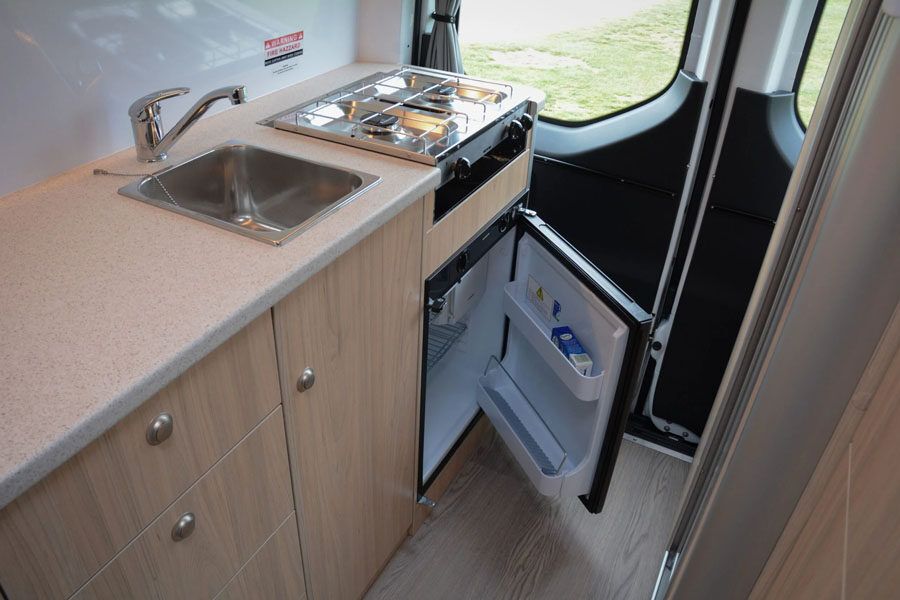 De keuken van de Pacific Horizon 2 plus 1 camper met een openstaande koelkast onder het gasfornuis