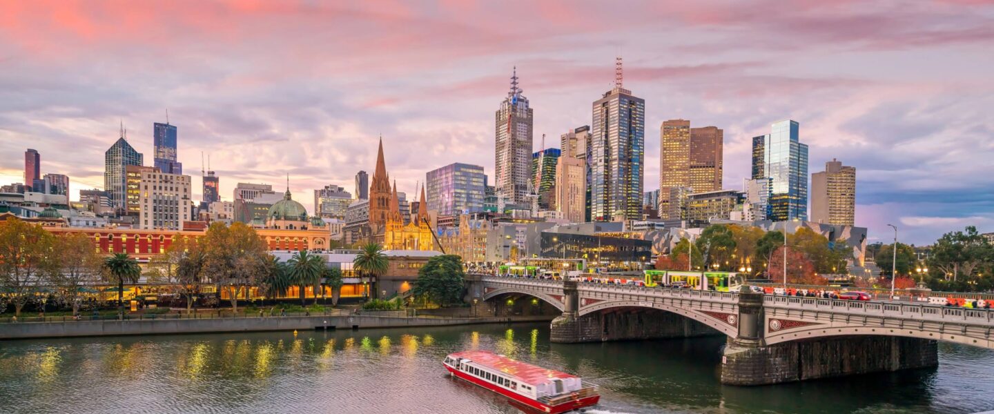 Rondvaartboot vaart bij de brug over de Yarra rivier in Melbourne bij zonsondergang met de skyline erachter