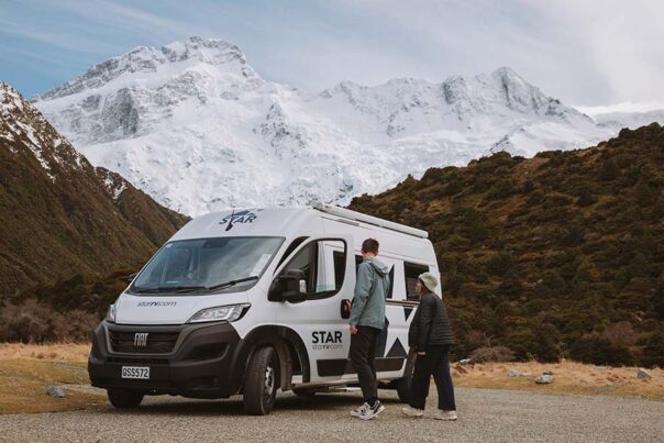 Een stel loopt naar de geparkeerde Star RV Polaris 2 camper met op de achtergrond besneeuwde bergtoppen
