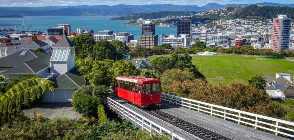 Zicht op Wellington en de zee vanaf de trambaan met een rode tram die naar beneden rijdt