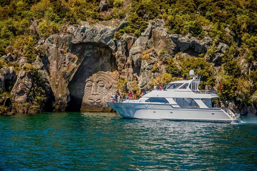 Een boot met toeristen vaart over Lake Taupo langs de Maori rock carving