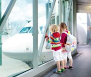Twee jonge kinderen kijken naar een vliegtuig van achter een raam op het vliegveld